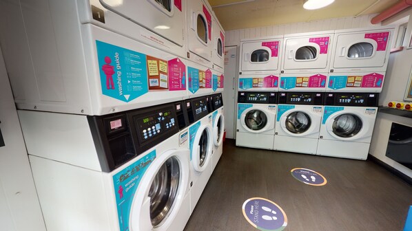 A laundromat with multiple washing machines and dryers, each with a user guide and safety instructions. - Daisy Bank - Campus Accommodation (Manchester)