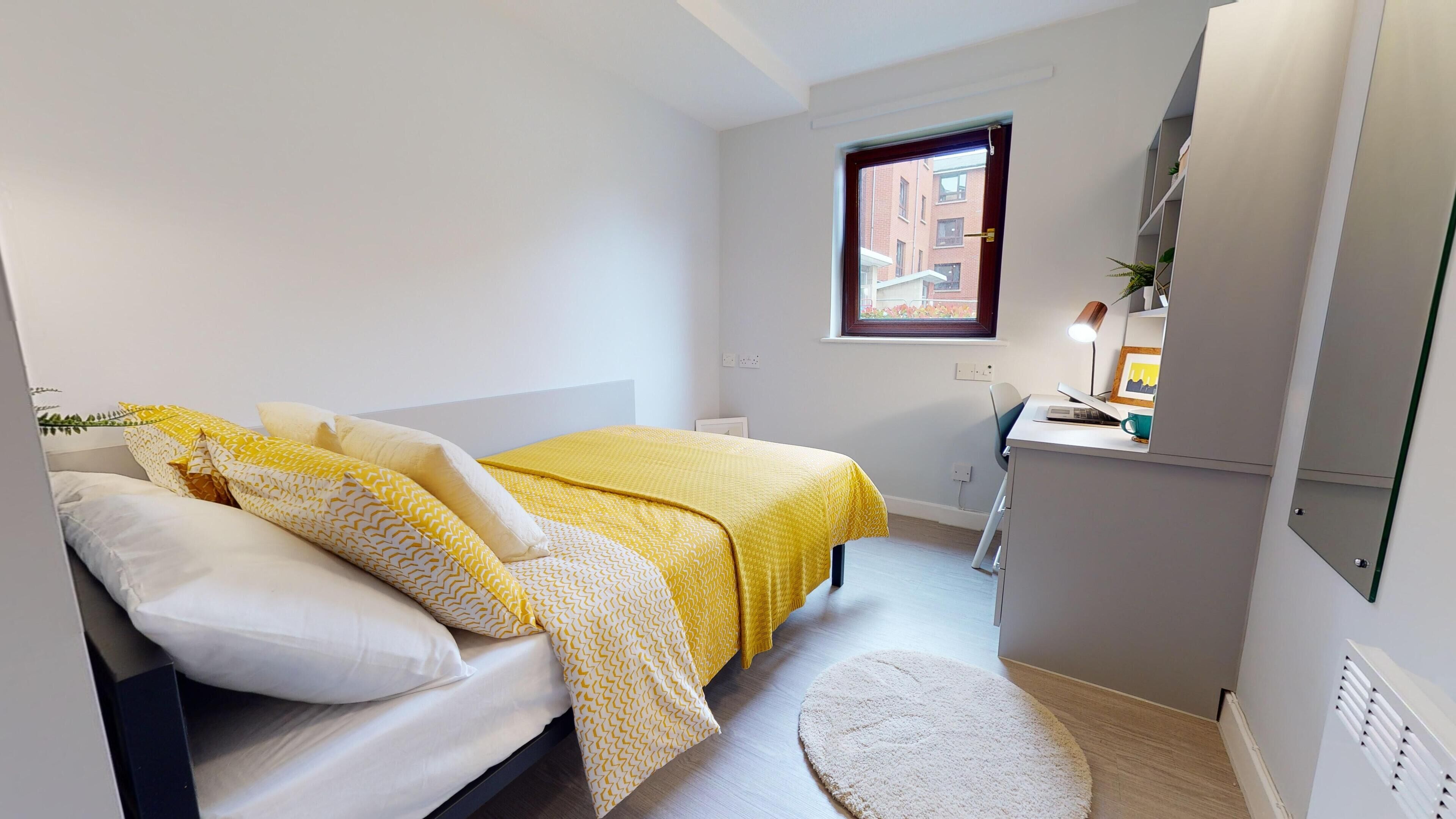 A small, modern bedroom with a bed, a desk, and a window.
