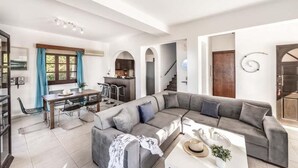 A spacious living area with a grey sectional sofa, a dining table with chairs, and a kitchen area visible through an archway. - Villa Argaka Vista - Three Bedroom Villa, Sleeps 6 (Argaka)