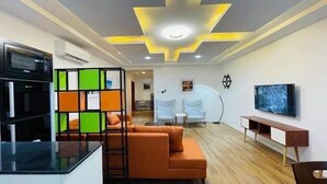 Una sala de estar moderna con un sofá, un televisor y una zona de cocina con un refrigerador y una máquina de café.