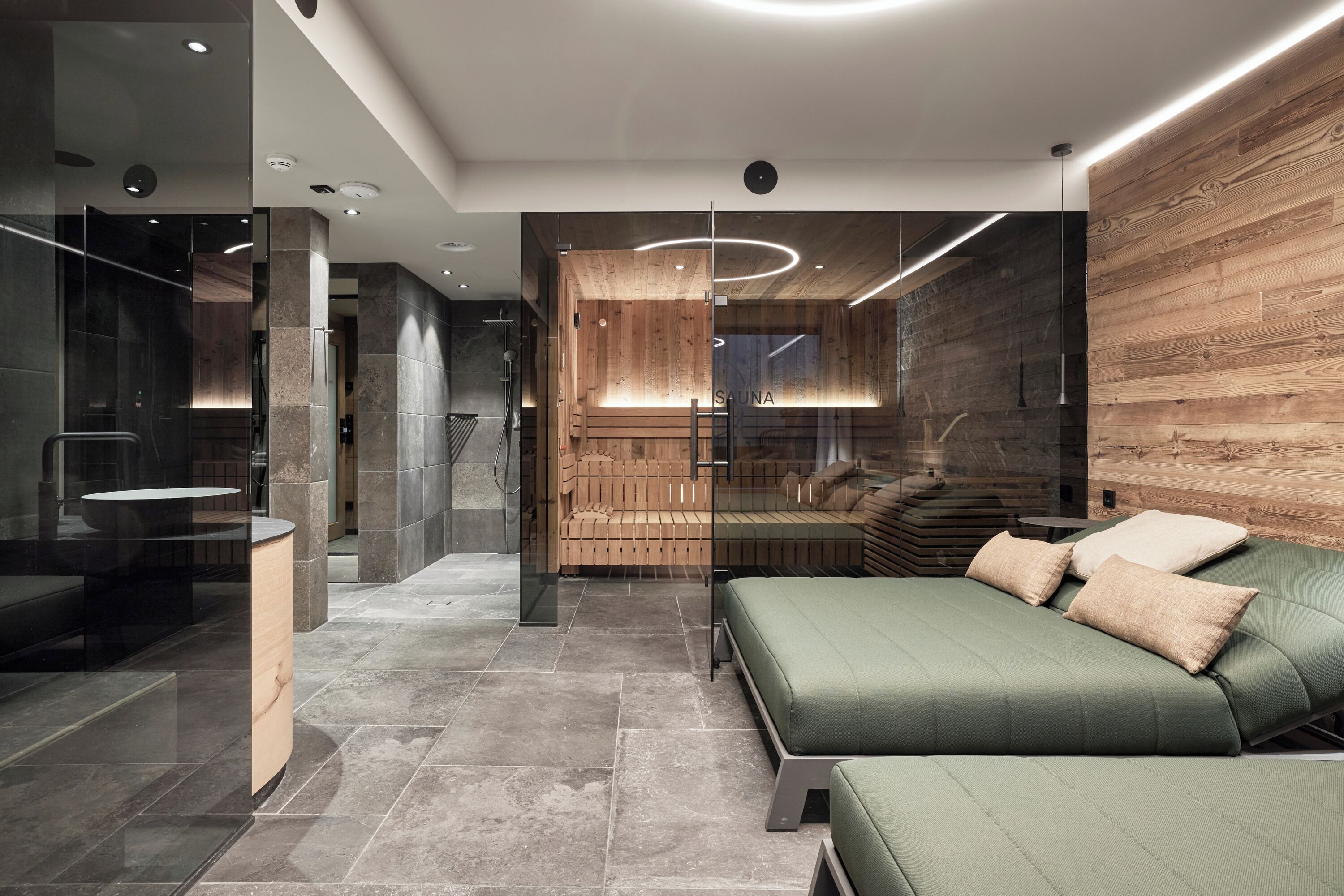 Un moderno cuarto de spa con una pared de madera, un sofá verde y un separador de vidrio.