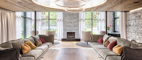 A modern living room with a stone fireplace, two sofas with cushions, a coffee table, and a wooden ceiling with a circular light fixture.