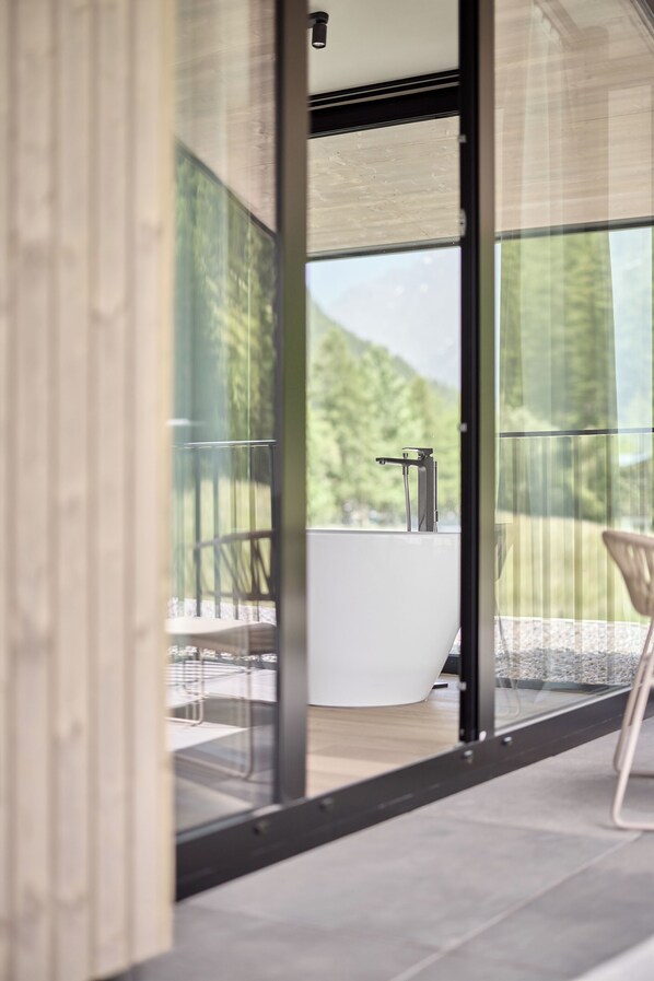A modern bathroom with a freestanding bathtub, a glass-enclosed shower area, and a view of a mountain landscape. - Chalet White Pearl by MYALPS (Soelden)
