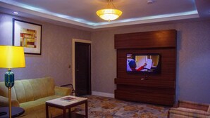 A living room with a sofa, a coffee table, a lamp, a television mounted on the wall, and a door. - Golden Vista Hotels (Owerri)