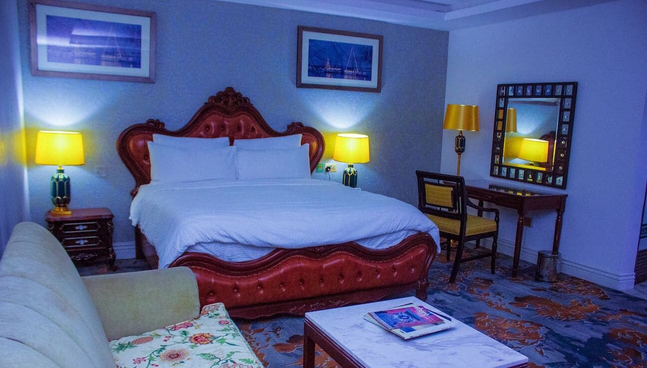 Une chambre d’hôtel avec un grand lit, deux lampes de chevet, une table de nuit en bois, une chaise, une petite table et un miroir au mur.