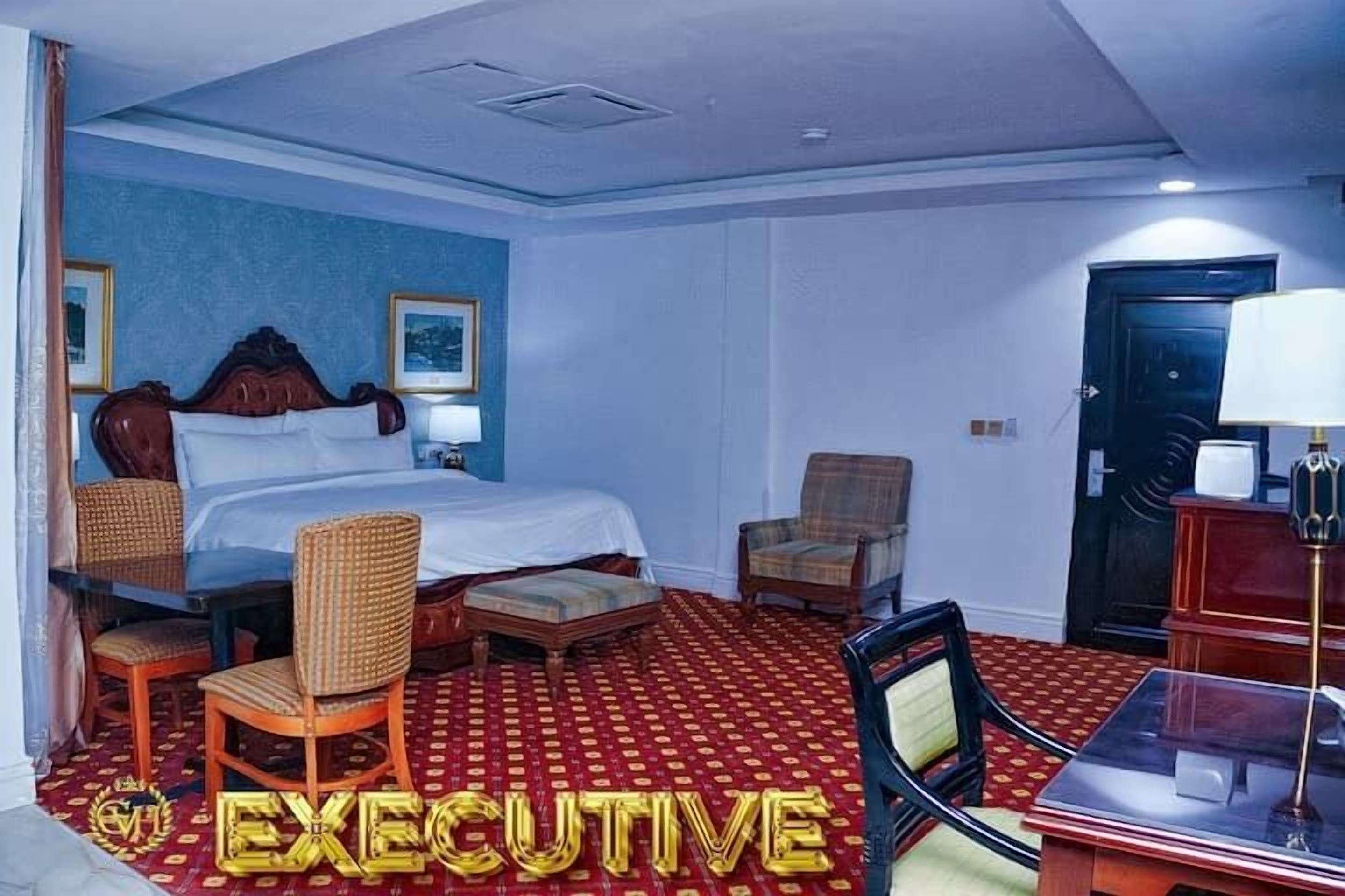 Una habitación de hotel con una cama grande, dos sillas, un escritorio y una alfombra roja estampada.