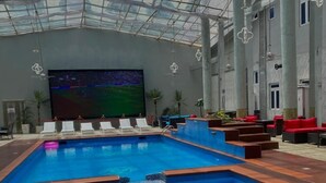 An indoor swimming pool with clear blue water, surrounded by lounge chairs and red cushions. - Golden Vista Hotels (Owerri)