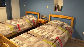 Une chambre avec deux lits simples, une table de chevet avec une lampe et une étagère murale avec des livres.