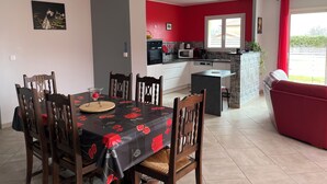 Un coin repas avec une table dressée pour six personnes, une cuisine en arrière-plan et un canapé rouge dans l’espace salon.