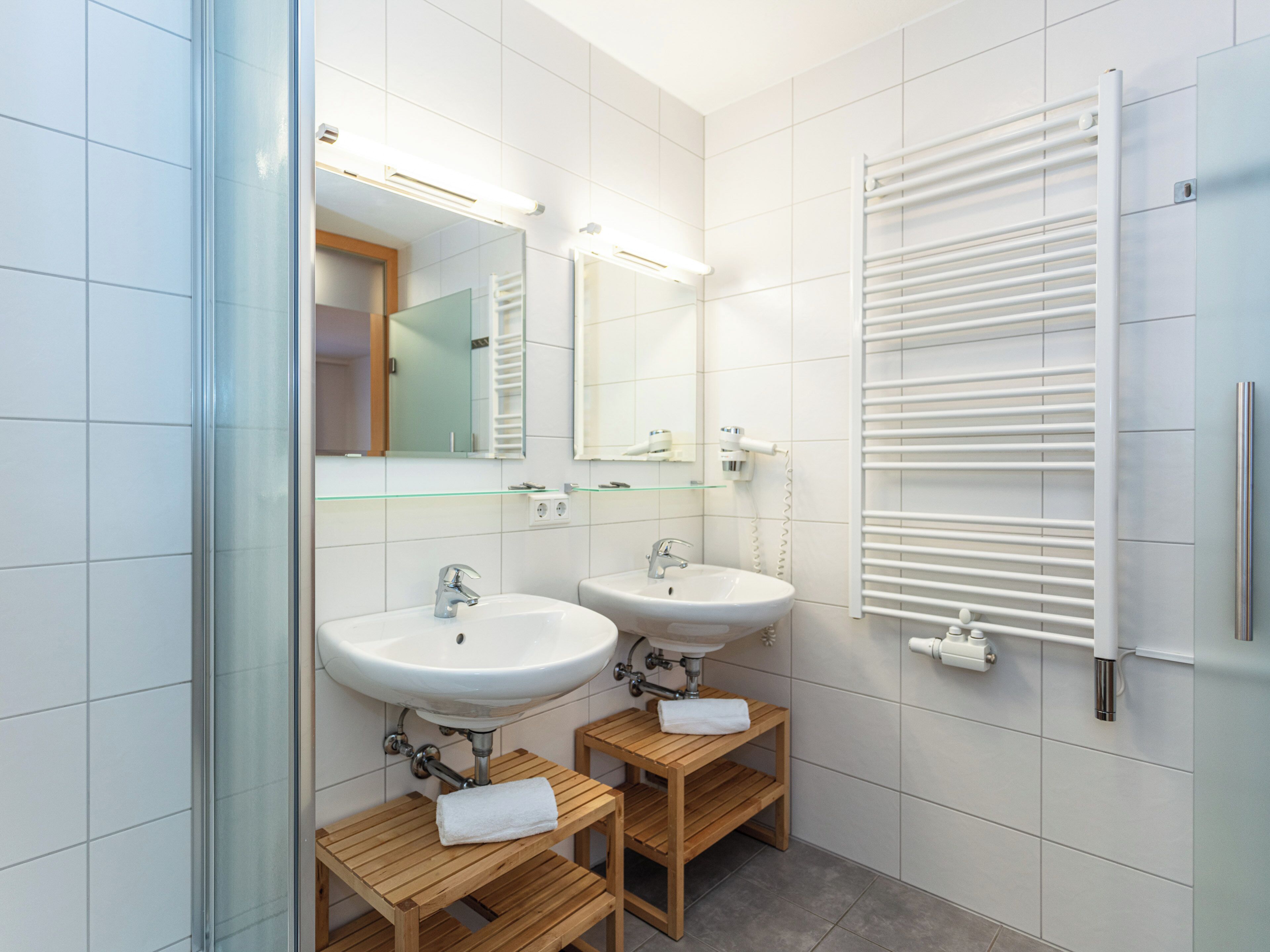 A modern bathroom with two sinks, a glass shower enclosure, and a towel rack.