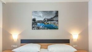 Una camera d'albergo con un letto, due cuscini, un comodino e un quadro appeso al muro raffigurante una scena di lago.