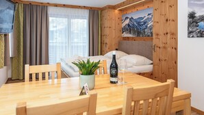 Una camera accogliente con un tavolo da pranzo in legno, sedie, un letto con lenzuola bianche, una pianta in vaso e una bottiglia di vino.