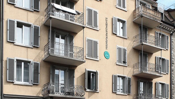 En bygning med flere etager og altaner, en indgang i stueplan med en grøn og hvid markise, og et skilt med teksten "VIAZIONE APARTMENTES".