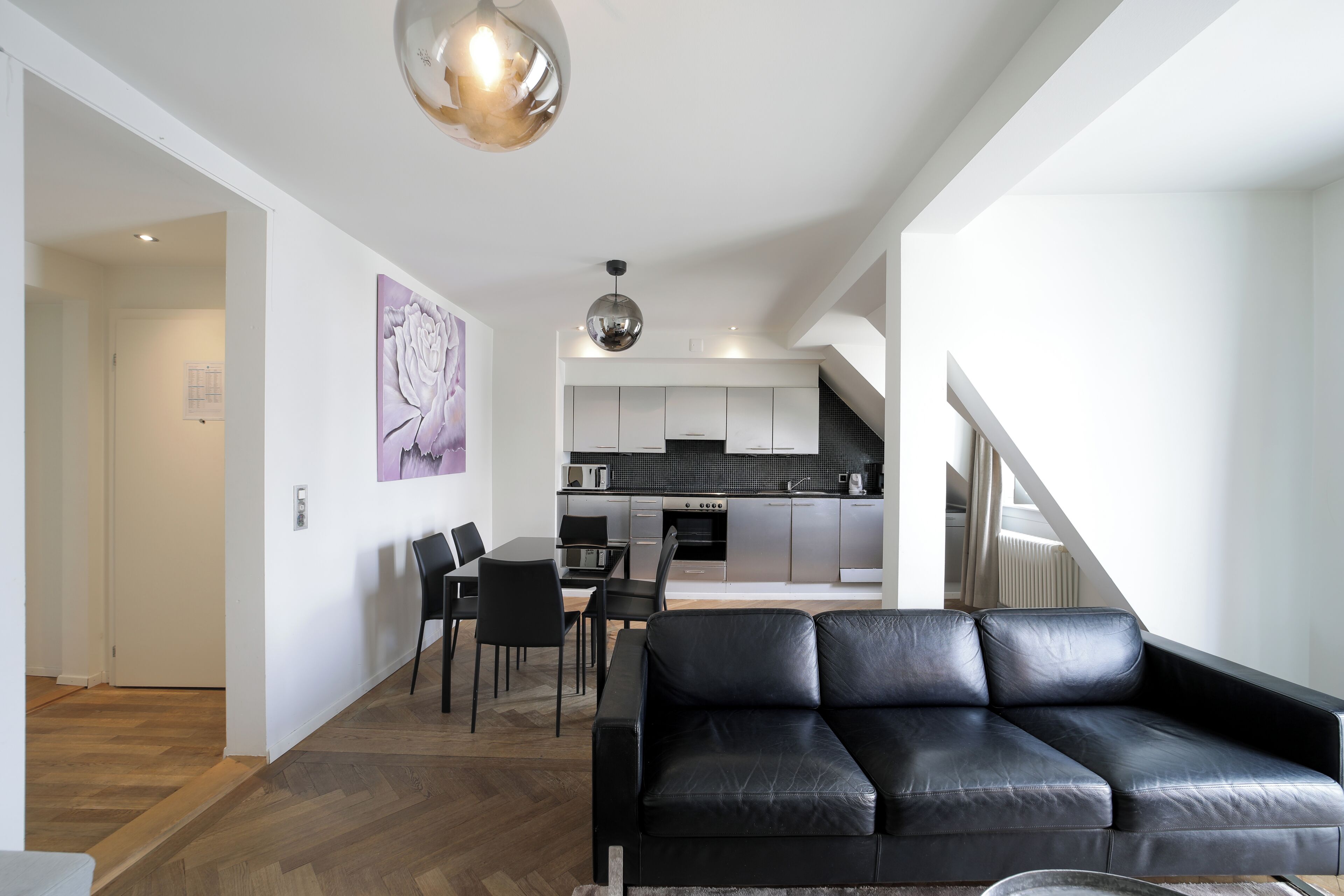 Ein modernes Wohnzimmer mit einer schwarzen Ledersofa, einem Essbereich mit Tisch und Stühlen sowie einer Küche mit zeitgemäßer Ausstattung.