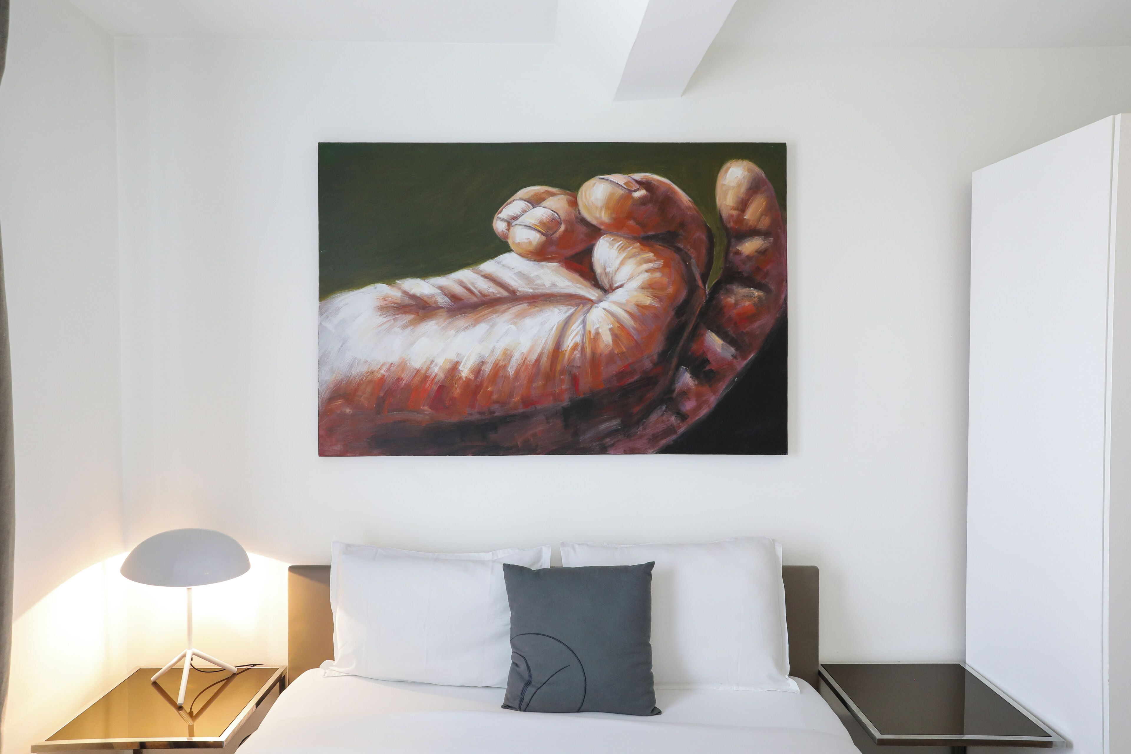 A bedroom with a bed, pillows, a bedside table, and a wall-mounted painting.