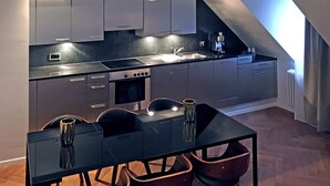 Et moderne køkken med sort bordplade, rustfrie stålapparater og et spiseområde med et sort bord og stole.