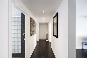 A hallway with a dark wooden floor, white walls, a large mirror, and a door at the end. - VISIONAPARTMENTS Zurich Hardstrasse (Zürich)