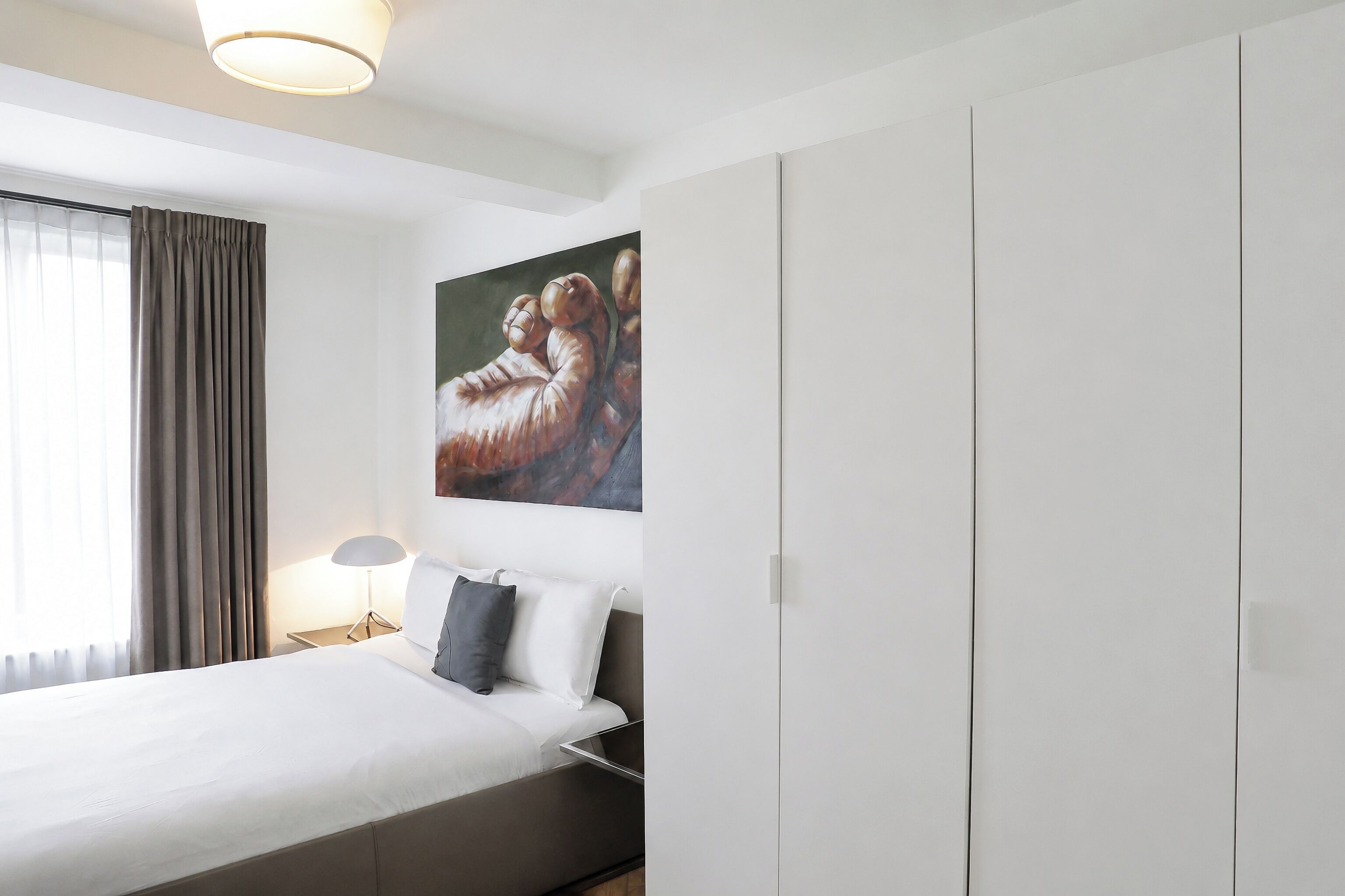 A hotel room with a bed, a nightstand, a lamp, a painting, and a wardrobe.