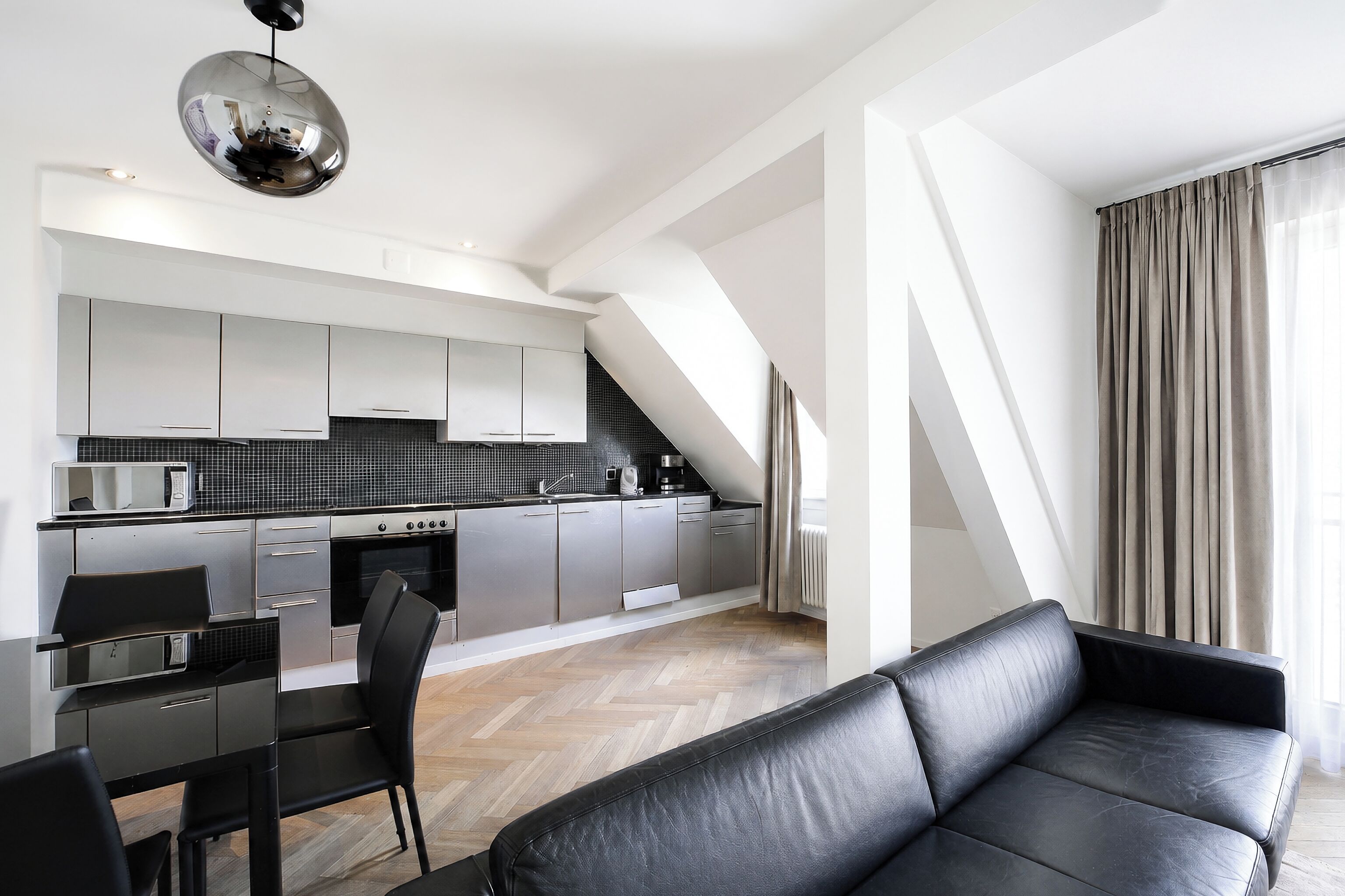 Eine moderne Küche mit weißen Schränken, einer schwarzen Arbeitsplatte und einem Essbereich mit einem schwarzen Tisch und Stühlen.