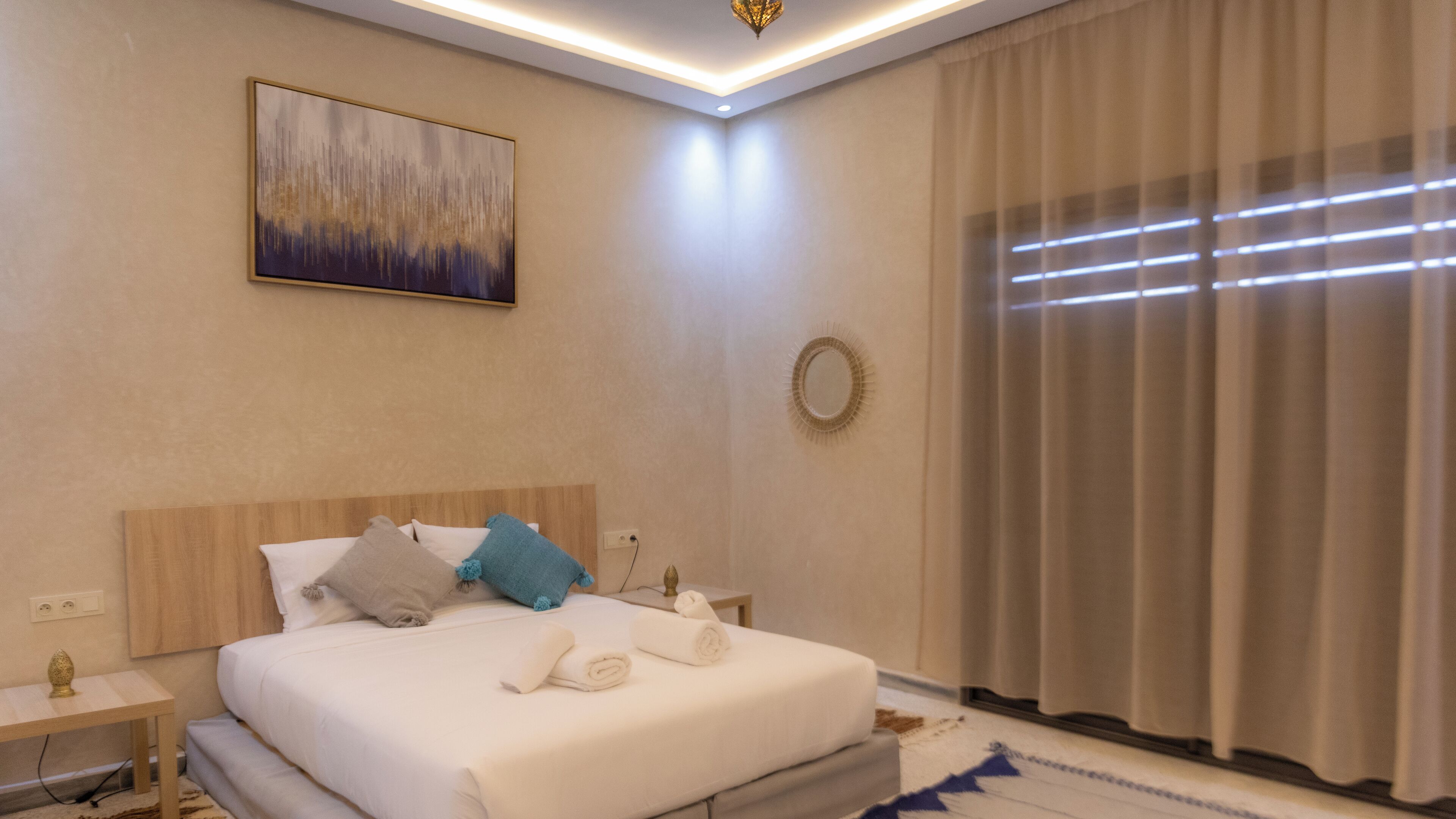 A neatly arranged hotel room with a bed, bedside tables, a wall-mounted mirror, and a large window with curtains.