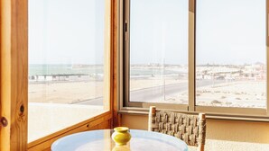 A wooden interior with a large window offering a view of a beach and cityscape. - The Ocean Villa  (Dakhla)