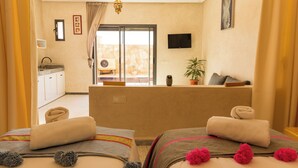 A hotel room with a balcony, a TV, a small table, and towels on the beds. - The Ocean Villa  (Dakhla)