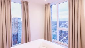 A hotel room with a large bed, two windows with curtains, and a city view. - The Blossoms (Croydon)
