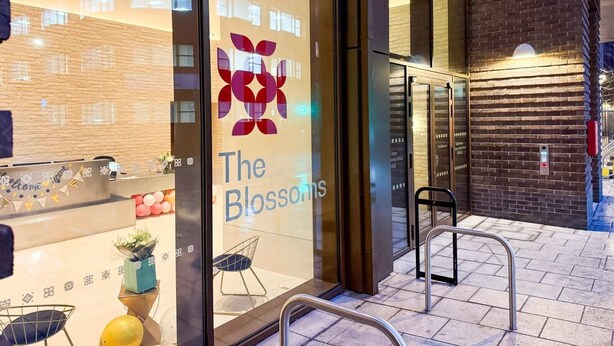 A hotel entrance with a glass door displaying 'The Blossoms' logo, a metal staircase, and a brick wall. - The Blossoms (Croydon)