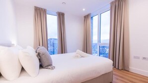 A modern hotel room with a large bed, beige curtains, and a city view. - The Blossoms (Croydon)