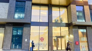 A modern building with a glass entrance, a visible logo, and a pedestrian crossing. - The Blossoms (Croydon)