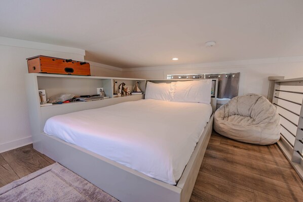 Un dormitorio con una cama grande, un sillón orejero, un aparador de madera y una estantería con diversos objetos.