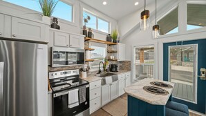 A modern kitchen with stainless steel appliances, white cabinetry, and a blue accent wall. - The Charming Chayil Cottage - 046 (Fredericksburg)