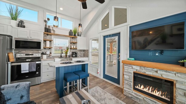 A modern kitchen with a central island, a built-in stove, and a stone fireplace. - The Charming Chayil Cottage - 046 (Fredericksburg)