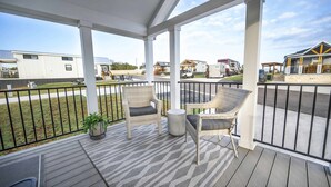 A covered outdoor area with wicker chairs and a small table, overlooking a residential area with mobile homes. - Bella Vista - 052 (Fredericksburg)