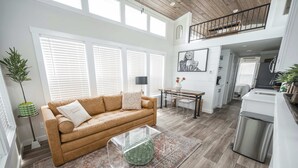 A spacious living area with a brown sofa, a clear glass coffee table, and a patterned rug. - Bella Vista - 052 (Fredericksburg)