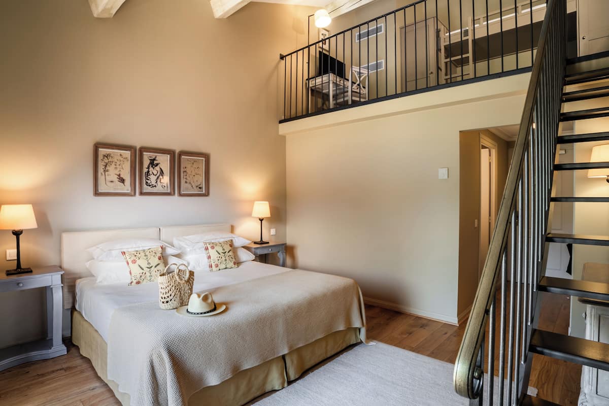 Ein Schlafzimmer mit Bett, Nachttischen, einer Lampe, einem Wandbild und einer Treppe.