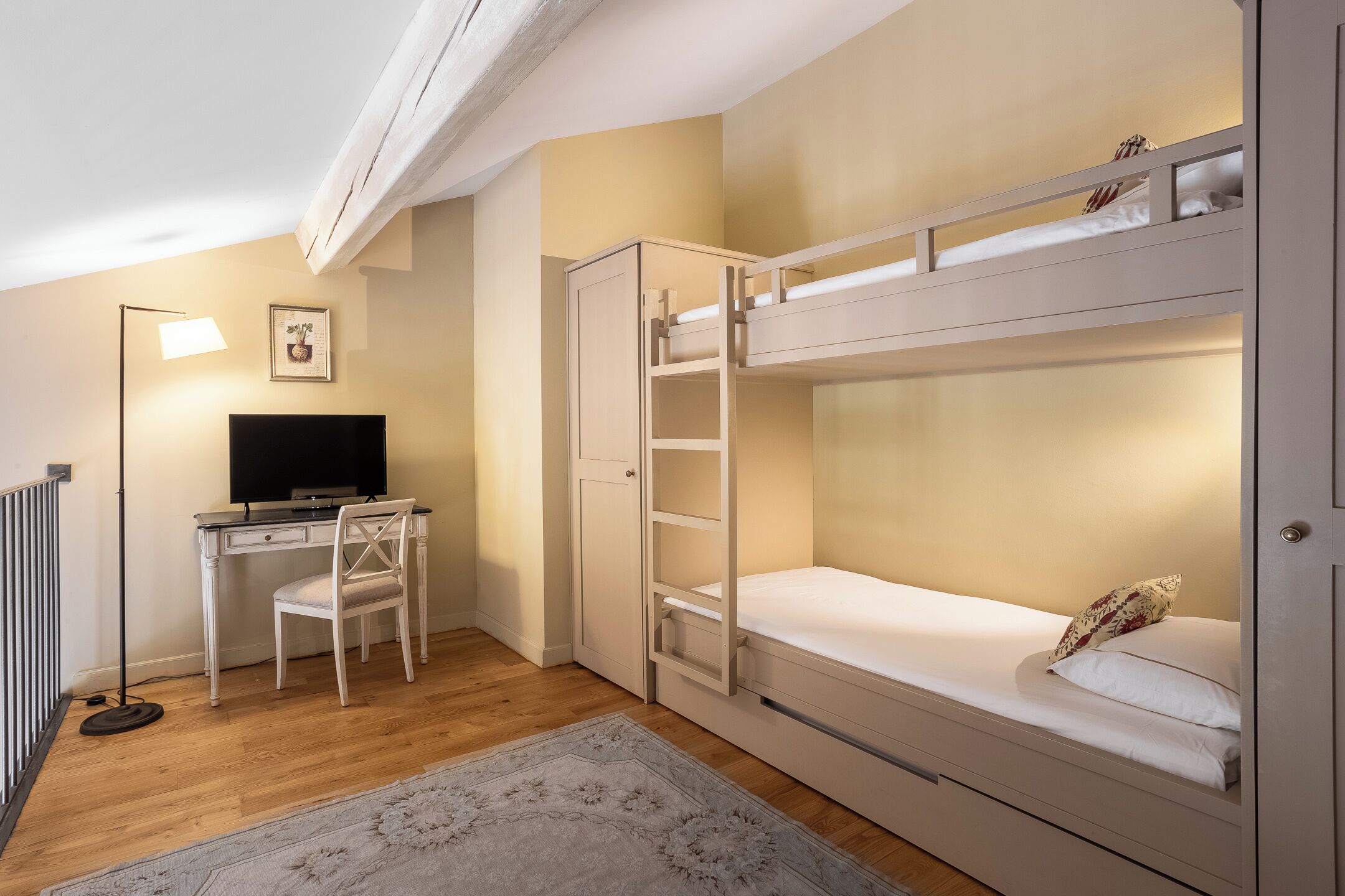 A room with a bunk bed, a desk with a chair, a television, and a radiator.