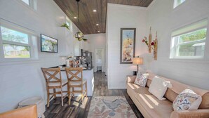 A spacious living area with a wooden ceiling, a kitchen in the background, and a large window providing natural light.