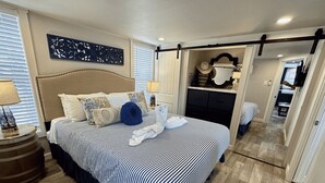 A hotel room with a large bed, a headboard, a bedside table with a lamp, a decorative wall piece, and a mirror.