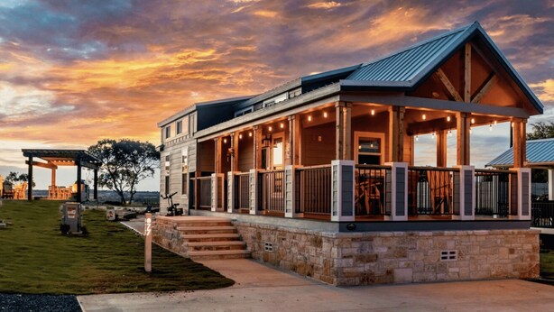 A modern house with a covered porch, stone foundation, and a view of the sky.