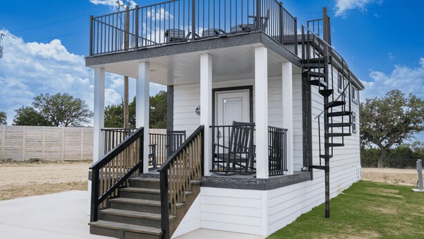 Une maison à deux étages dotée d’un porche couvert, d’un escalier et d’un petit espace extérieur aménagé pour s’asseoir.