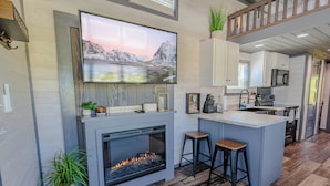 A modern kitchen with a large TV, a fireplace, bar stools, and a kitchen island.