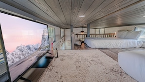 A bedroom with a large window, a bed, a desk, and a ceiling fan.