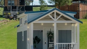 A small, single-story building with a porch, a door with a wreath, and a trash can.