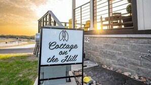 A sign for "Cottage on the Hill" with a view of the building's exterior and a sunset in the background. - Cottage on the Hill - 114 (Fredericksburg)