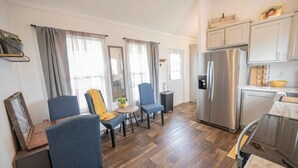 Una cocina moderna con refrigerador de acero inoxidable, piso de madera y una zona de comedor con sillas azules y una mesita.
