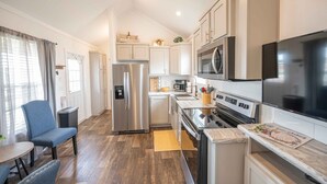 Una cocina moderna con electrodomésticos de acero inoxidable, una zona de comedor con una silla azul y suelo de madera.