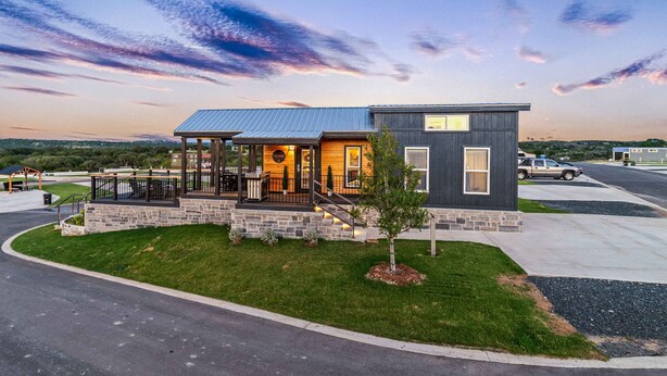 A modern two-story house with a covered porch, stone foundation, and a small tree in the front yard. - Comfortably Numb - 119 (Fredericksburg)