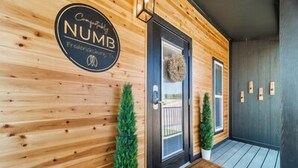 A wooden exterior wall with a circular sign reading "Comfortably NUMB" and a door with a wreath. - Comfortably Numb - 119 (Fredericksburg)