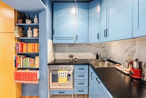 Une cuisine avec des meubles de rangement bleus, une cuisinière, un évier et une bibliothèque remplie de livres.